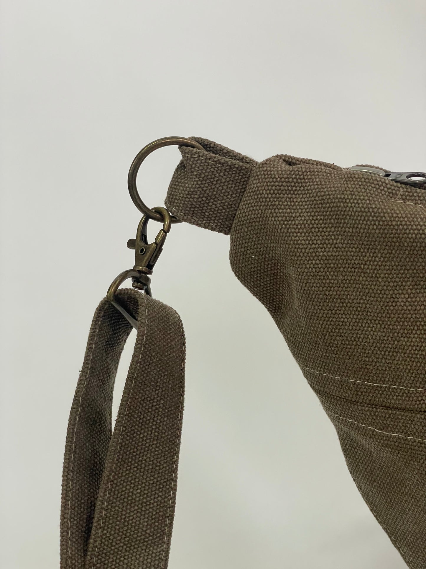 Close up of Brown sling bag with topstitching, brass hardware and YKK zips,