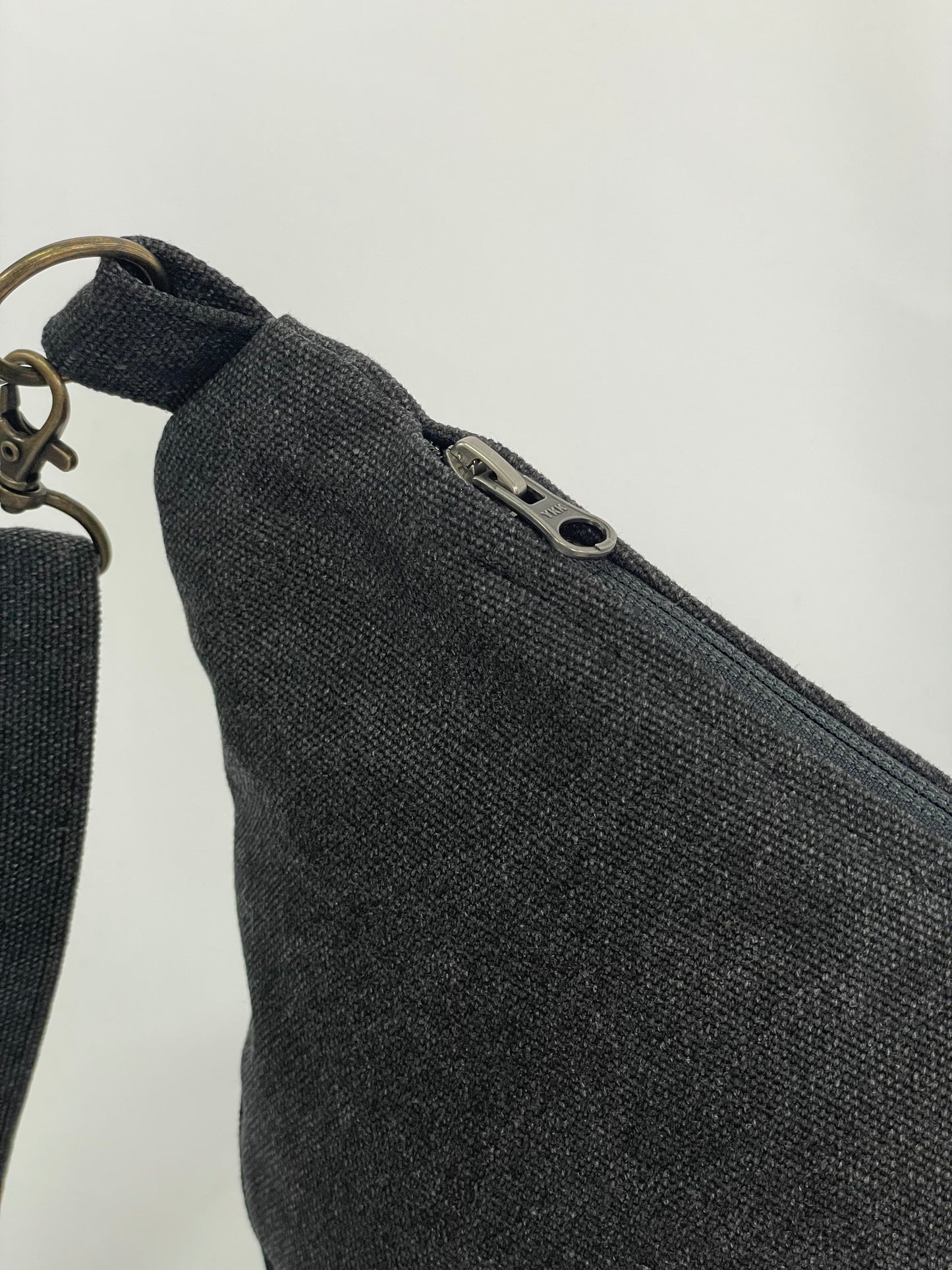 Close up of Black sling bag with topstitching, brass hardware and YKK zips