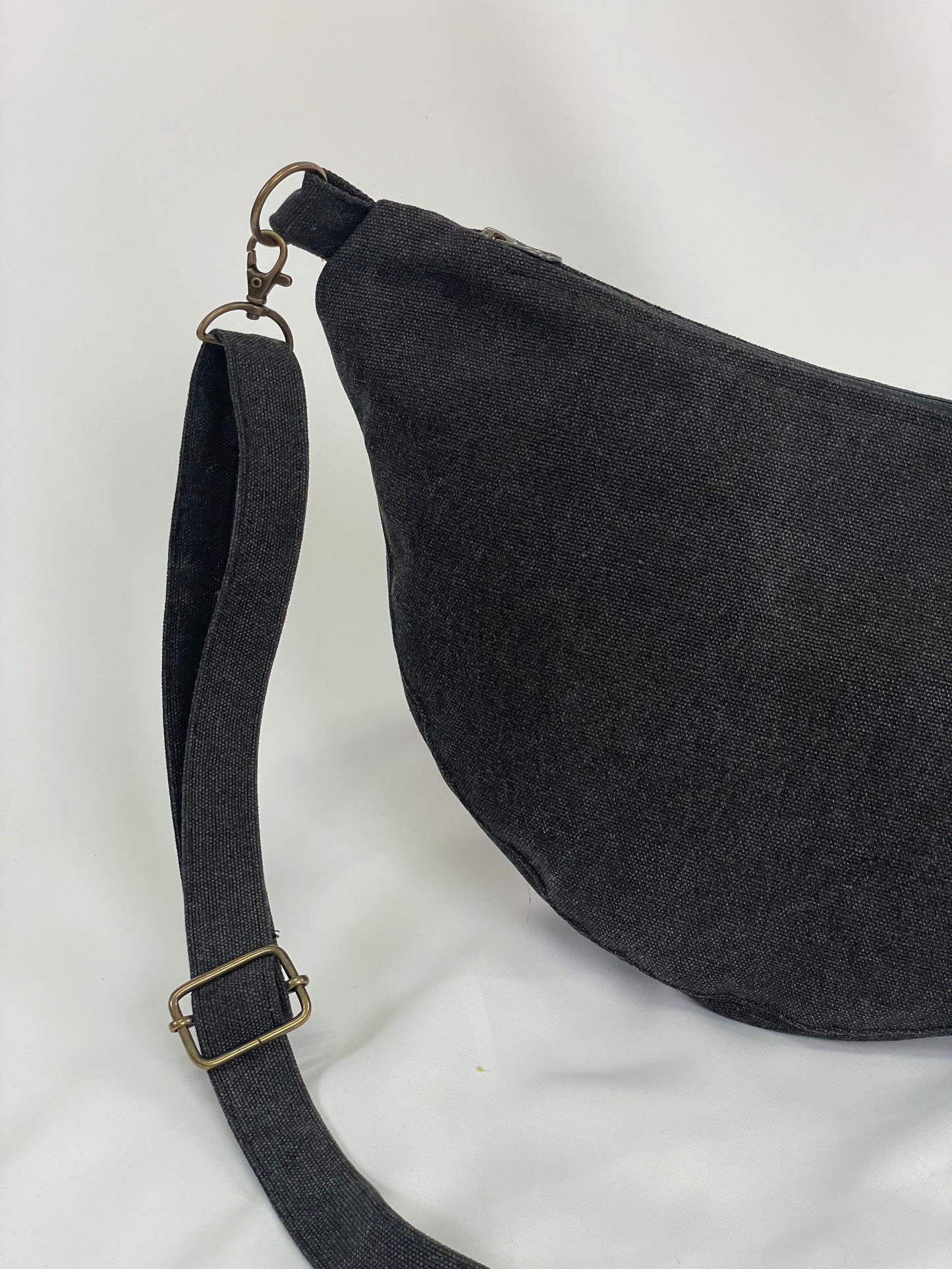 Close up of Black sling bag with topstitching, brass hardware and YKK zips
