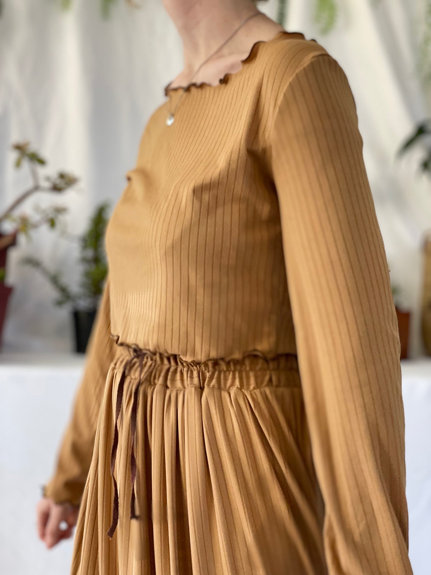 Model wears matching skirt and top set. The model stands in front of a white backdrop with pot plants.