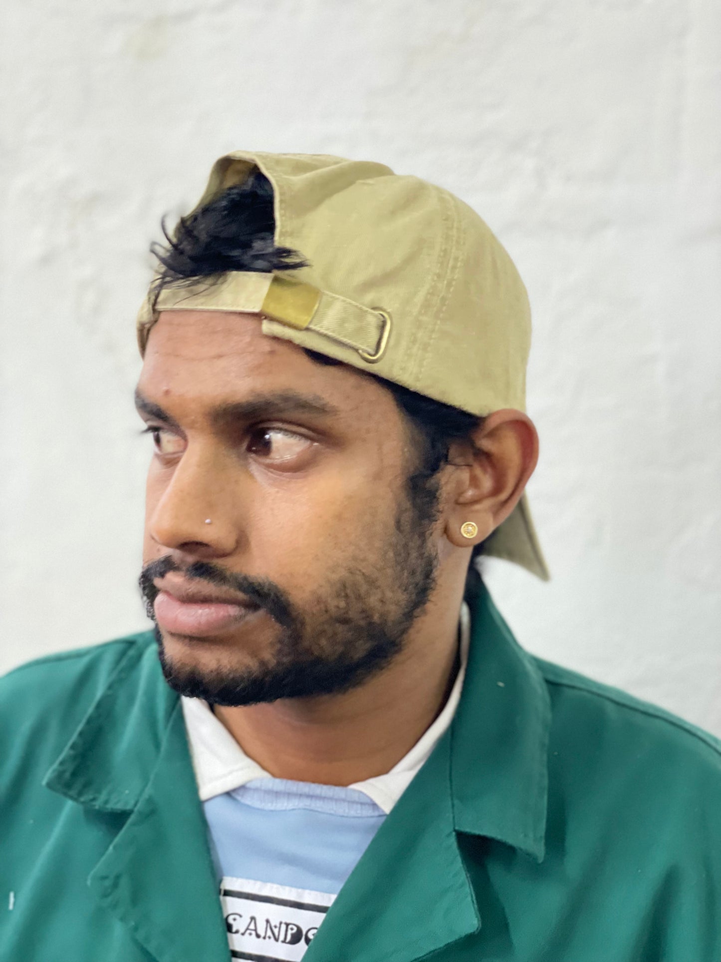 Model wears stone coloured peak cap backwards whilst looking to the side.