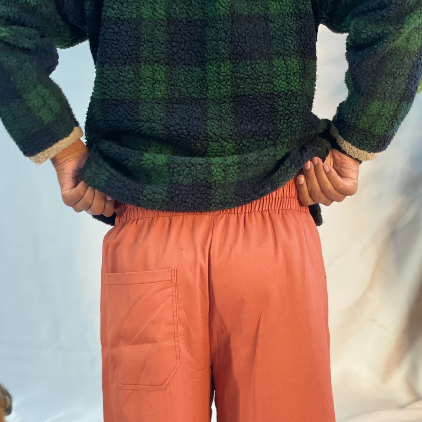 Model wearing rust coloured pants with a wool plaid jersey against a white backdrop.