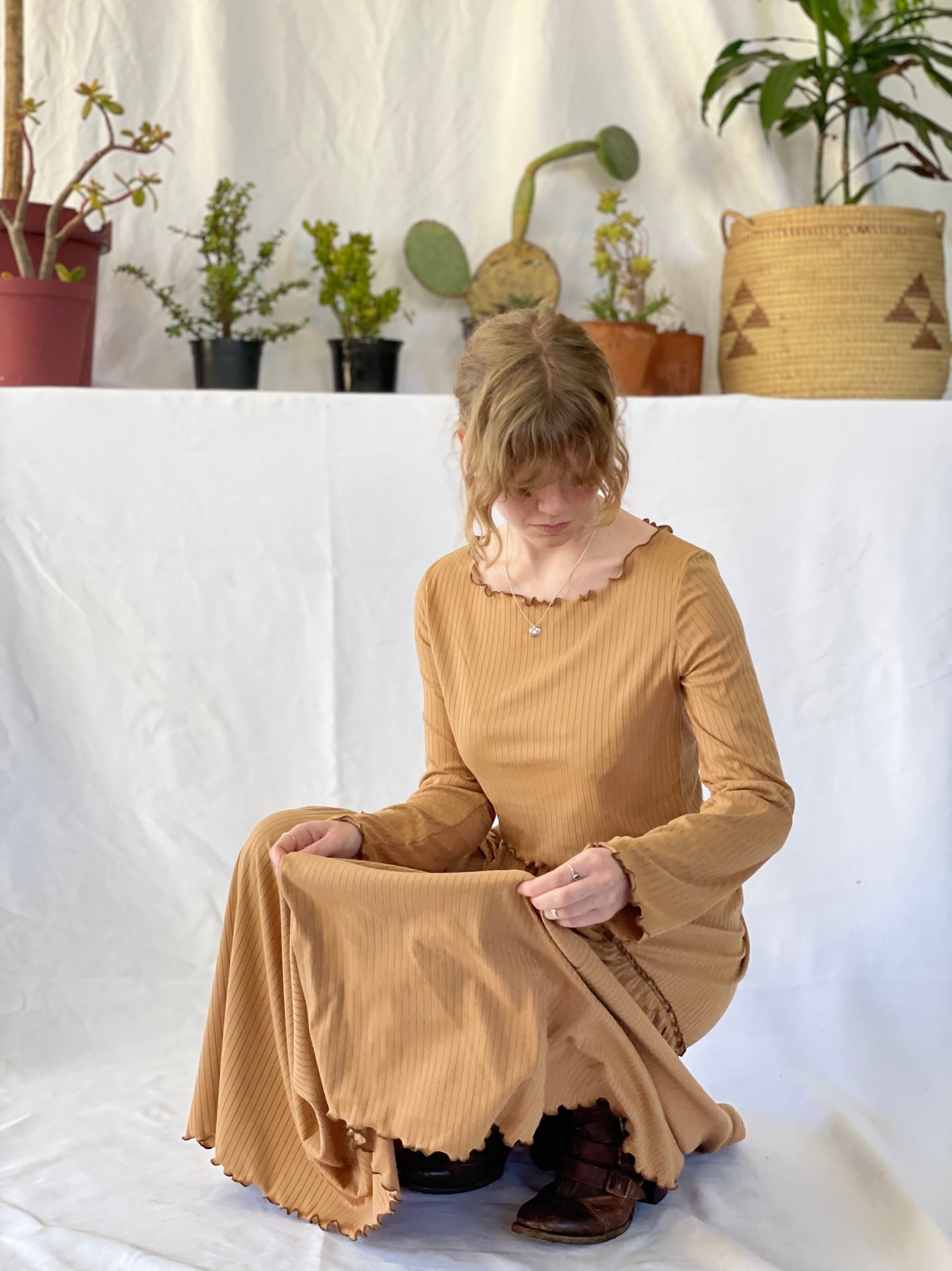 Model wears matching skirt and top set with brown boots. The model stands in front of a white backdrop with pot plants.