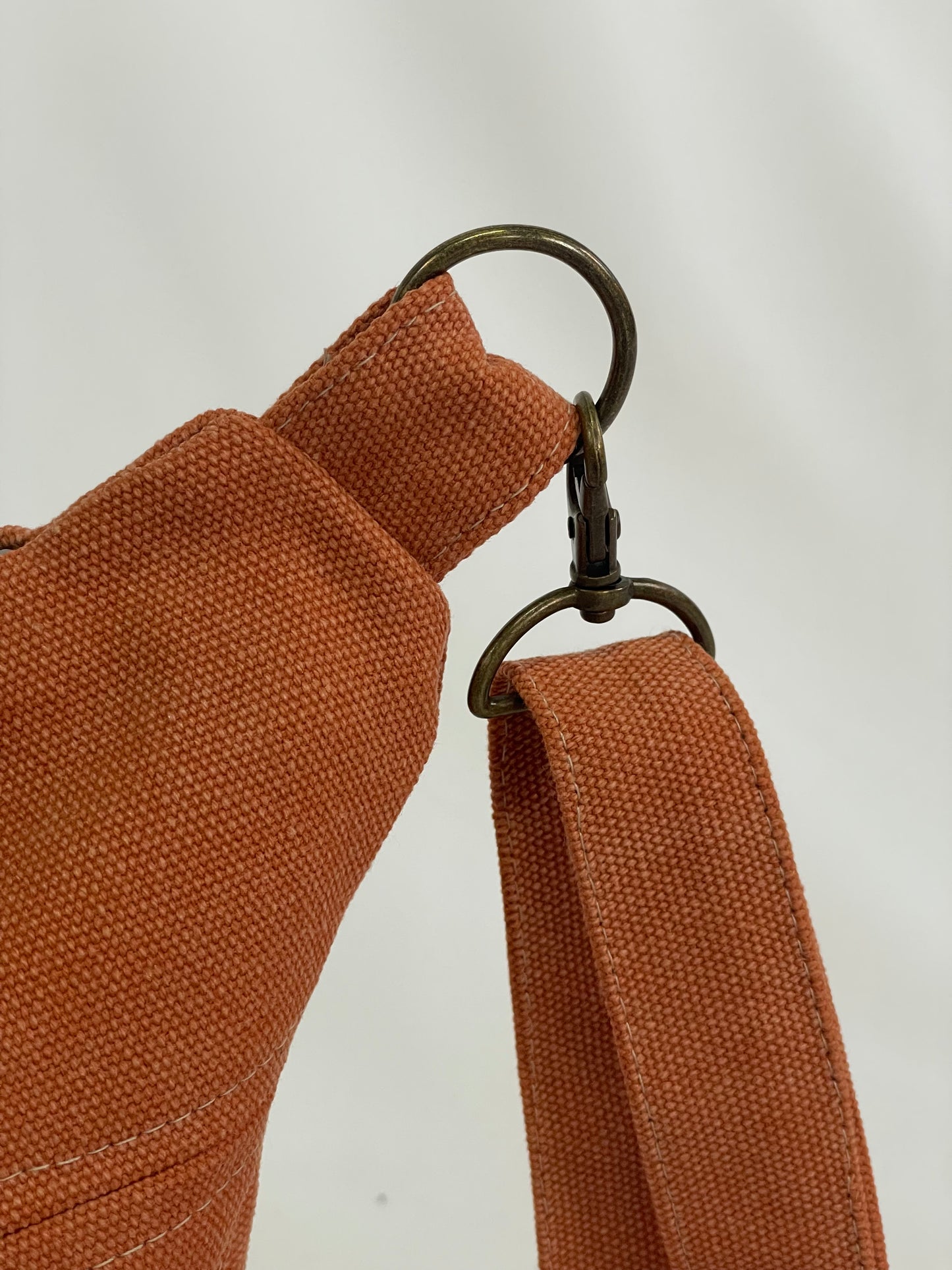 Close up of orange sling bag with brass hardware.