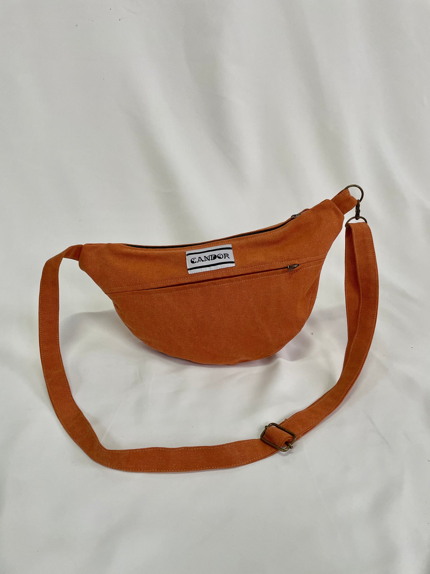 Orange sling bag with topstitching, brass hardware and YKK zips against a white backdrop.
