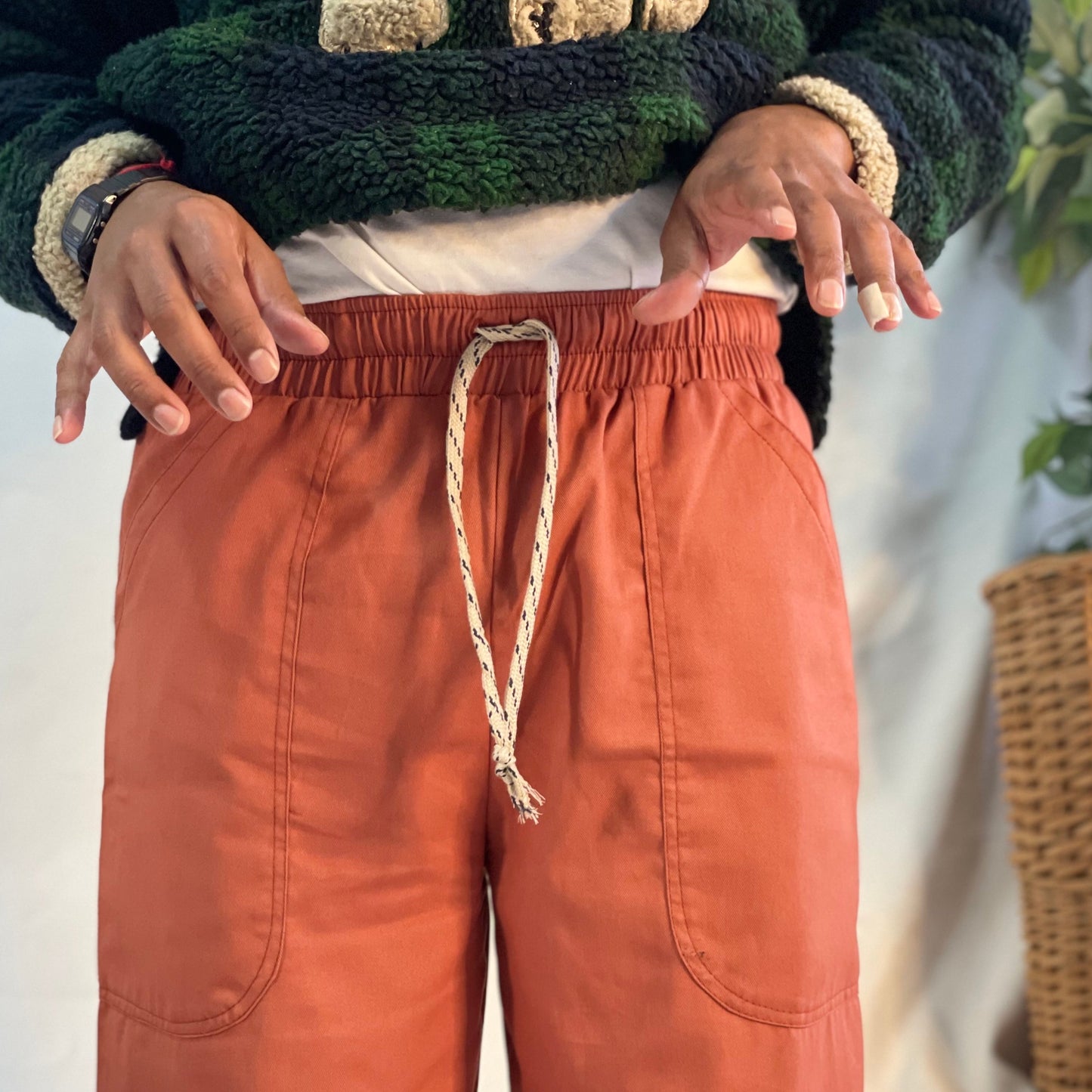 Model wearing rust coloured pants with a wool plaid jersey against a white backdrop.