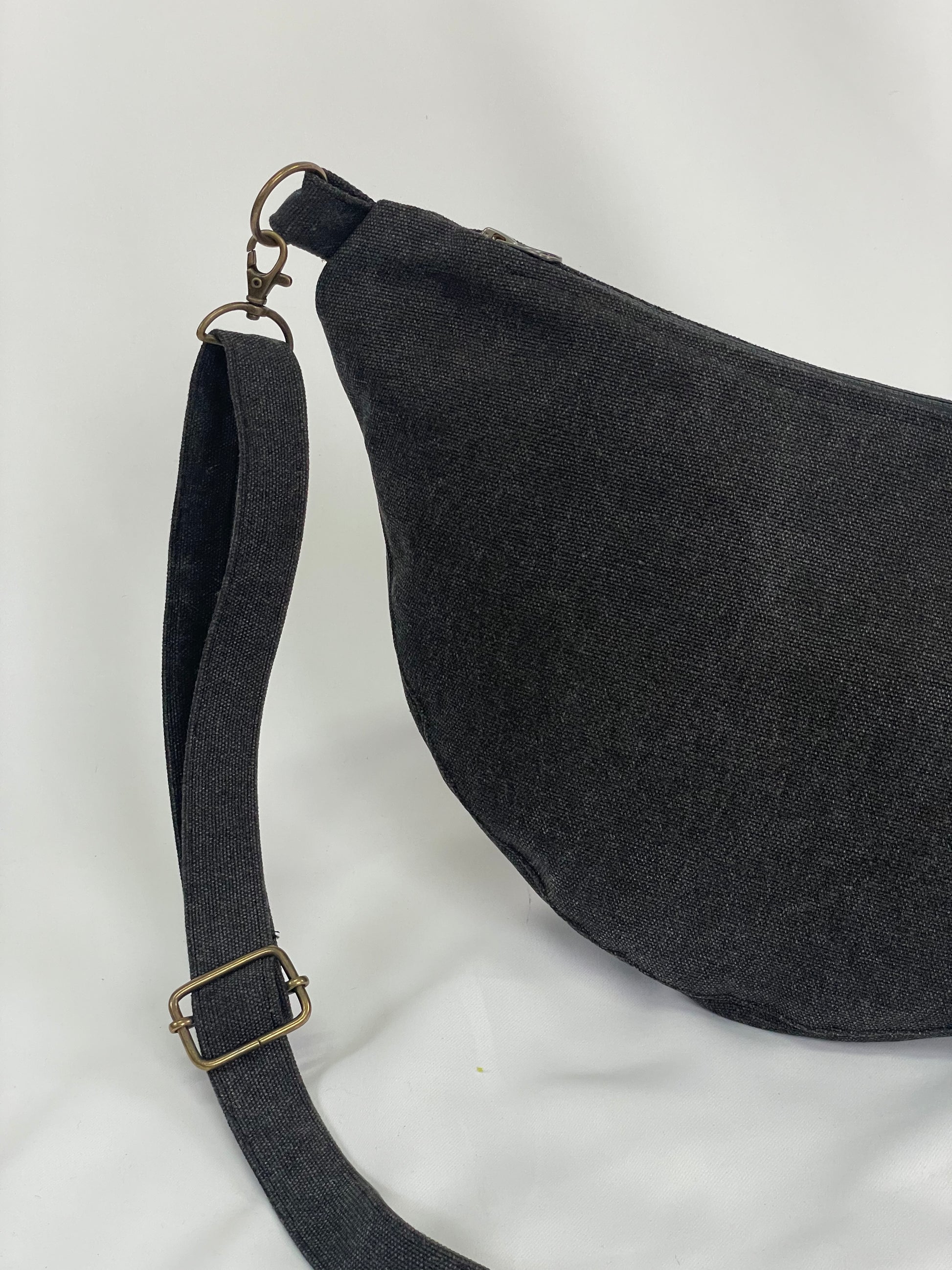 Close up of Black sling bag with topstitching, brass hardware and YKK zips
