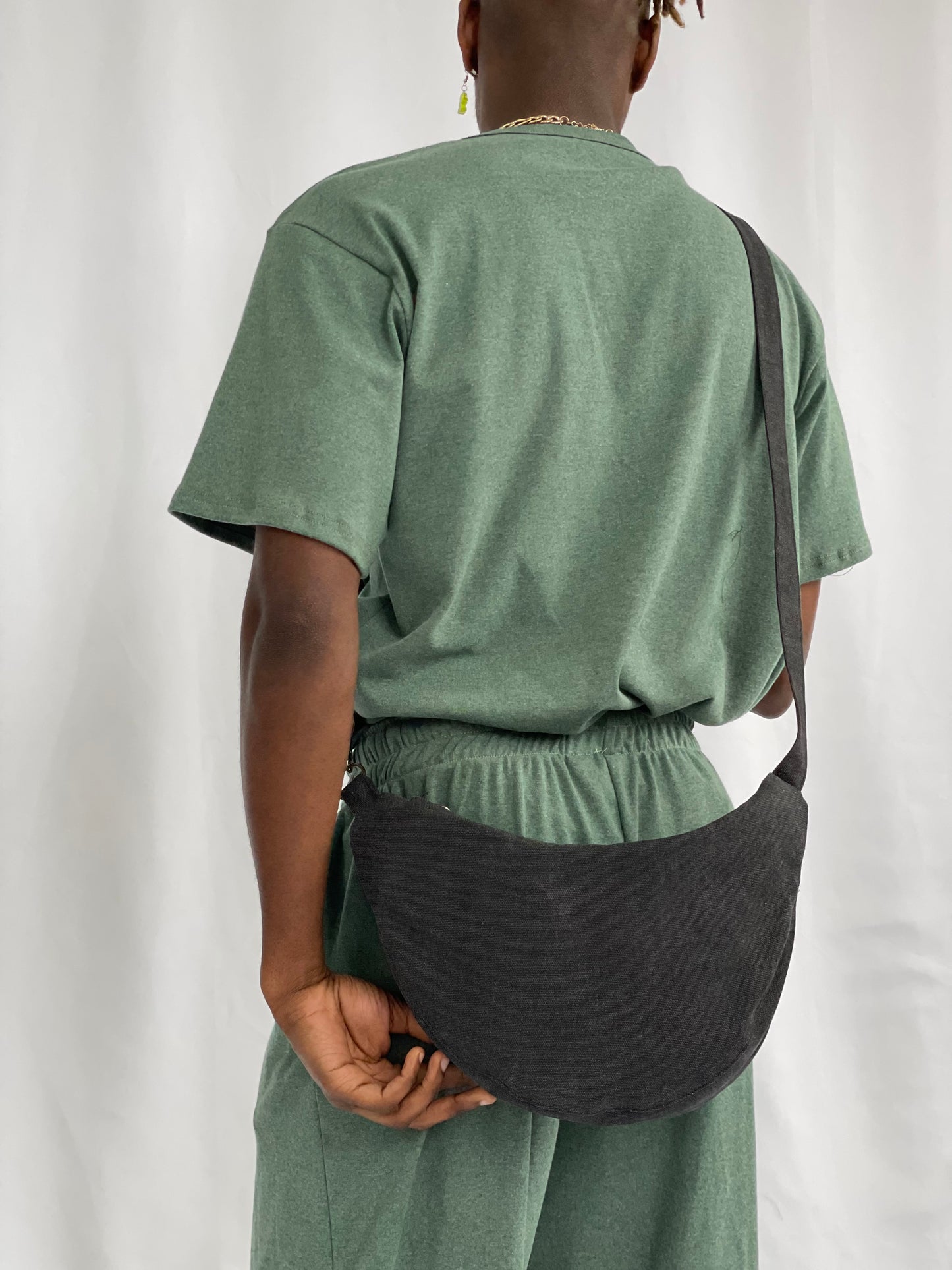 Models wears black sling bag cross body with green pants and t-shirt against a white backdrop 