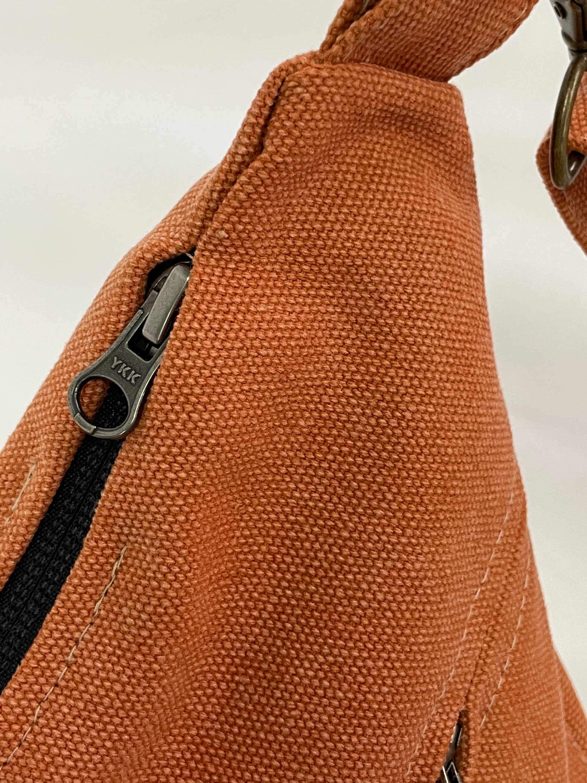 Close up of orange sling bag with YKK zips. 