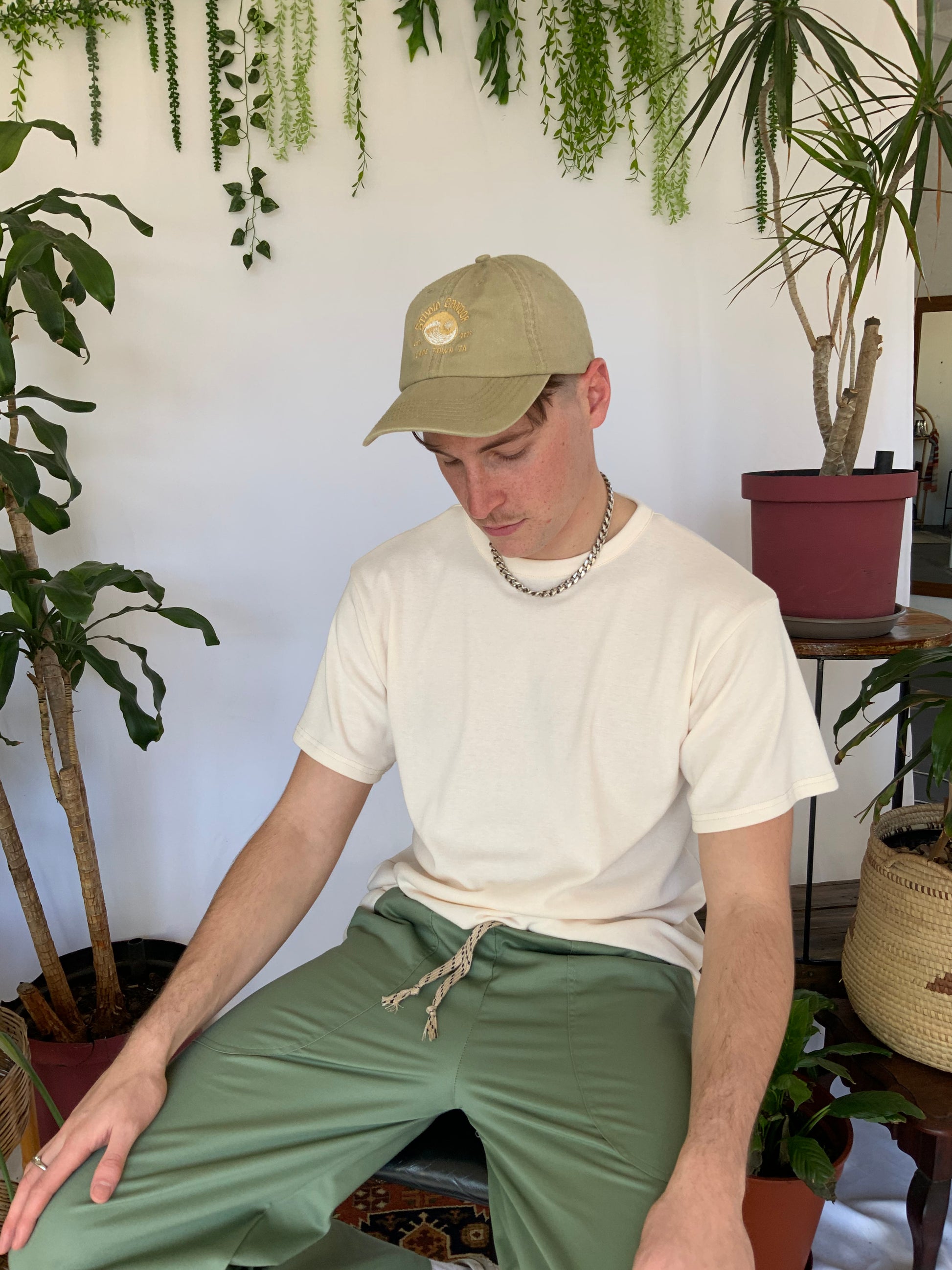 Models wears a stone coloured peak cap with a cream t-shirt and green pants.