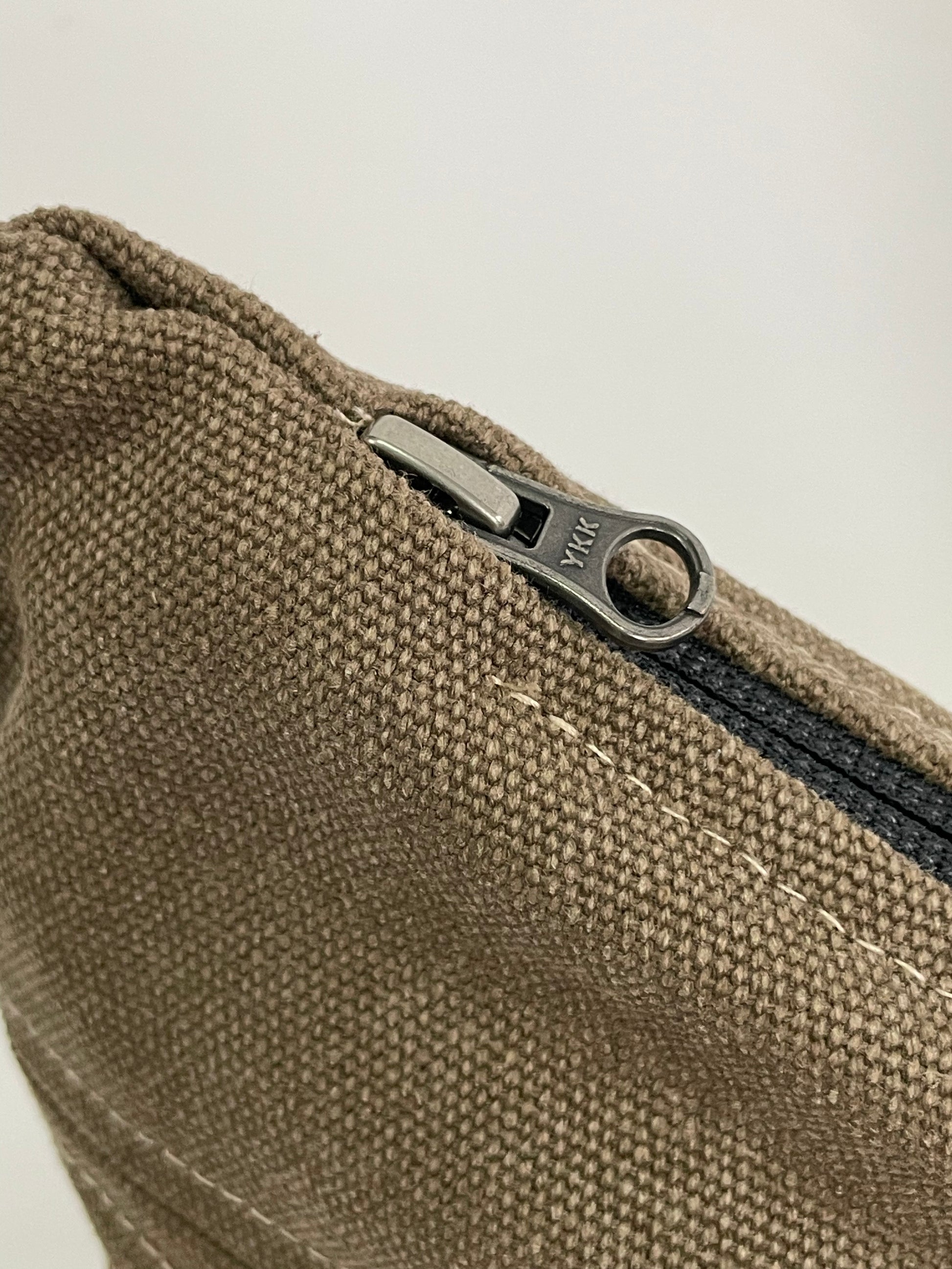 Close up of Brown sling bag with topstitching, brass hardware and YKK zips,