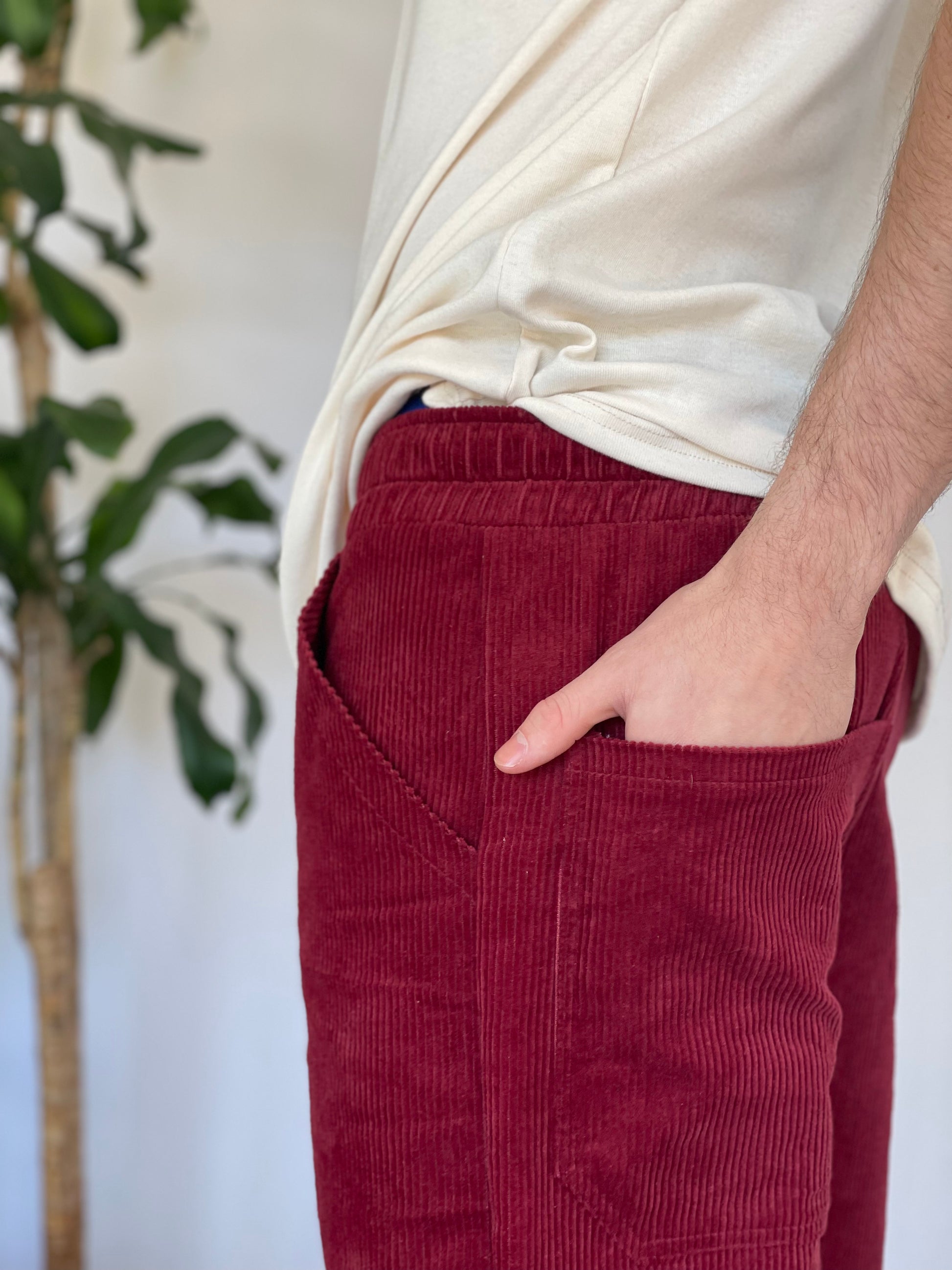 Close up of models hand in back pocket. Models wears burgundy corduroy pants and a cream t-shirt
